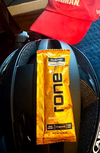 Customer's packet of Classic SuperCharged Honey resting on a black bike helmet next to a red Ironman visor.