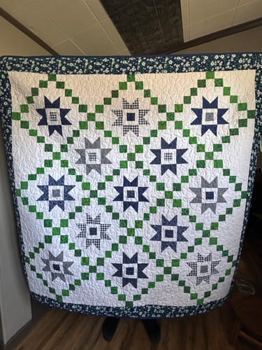Customer's completed Stars and Chains quilt, featuring navy star blocks, green chain patterns, and a floral border.