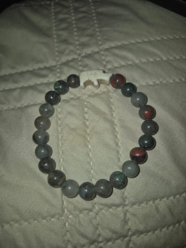 Customer's Charge Bracelet with dark stone beads and a white rhino charm on a bed.