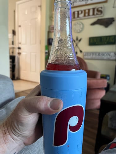 A customer holds the light blue Philadelphia Phillies Universal Buddy, which is keeping a glass bottle cool in their living room.
