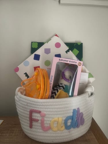Customer's personalized Baby Knits cotton basket with the name Fiadh in colorful stitched letters, filled with gifts.