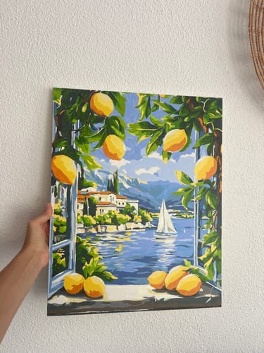 Customer's Malen nach Zahlen Lago & Zitronen painting, held by a hand, showing a coastal landscape with a sailboat.
