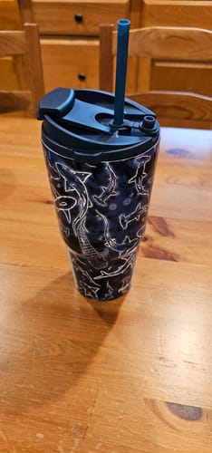 Customer's Midnight Reef To-Go Buddy tumbler with a dark shark pattern and a blue straw on a wooden table.