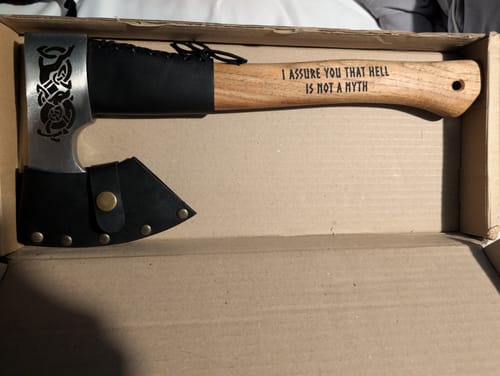 Customer's Urvangr camping axe in a cardboard box, featuring an engraved wooden handle and a black leather blade cover.