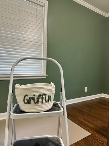 Customer's white knitted Baby Knits personalized basket with the name Griffin in green, sitting on a small step ladder.