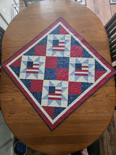 Customer's completed Land of Liberty quilt kit centered on a wooden table, featuring patriotic star and flag designs.