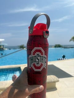 Reviewer holding a red Ohio State Bottle Buddy near a sunny pool