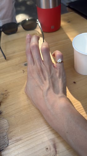 Customer's hand wearing the gold Pia ring on their pinky finger, set against a wooden table background.