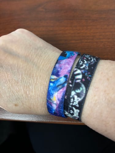 Customer's wrist wearing two colorful Trash Pandas Mystery Bracelets with vibrant raccoon patterns.