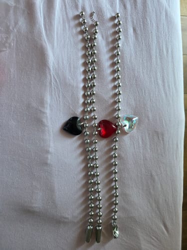 Customer's three beaded necklaces with black, red, and clear heart-shaped pendants resting on a light fabric surface.
