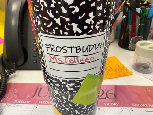 Customer's To-Go Buddy cup featuring a composition notebook pattern with a personalized label, sitting on a desk.