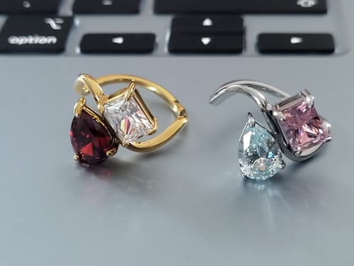 Customer's two Navae Birthstone Rings, one gold and one silver, with pear and rectangle-cut stones on a laptop.