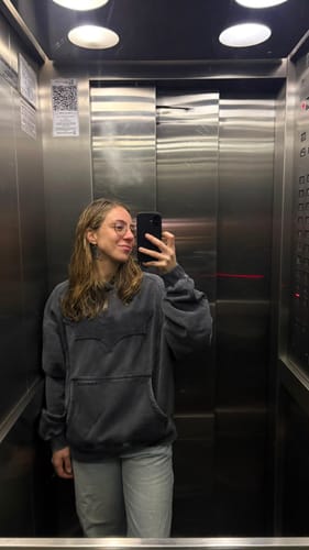 Customer's Batman Stealth Hoodie in an elevator mirror selfie, showing the tonal bat emblem and oversized fit.