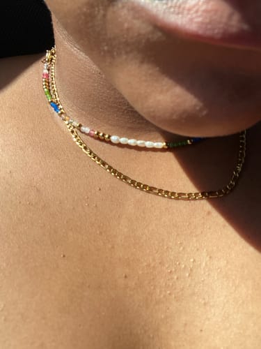Customer's gold Positano Necklace layered with a beaded necklace on their neck.