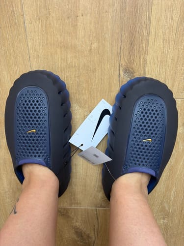 Customer's Nike Mind 001 Bleu Noirci slides on feet, featuring a perforated design and attached product tag.