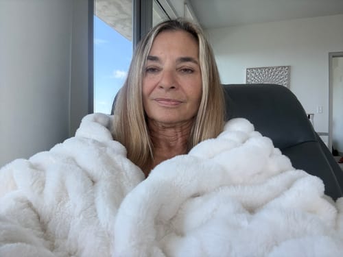 Reviewer looking comfortable while enveloped in the soft, fluffy Hugs Cream Blanket.