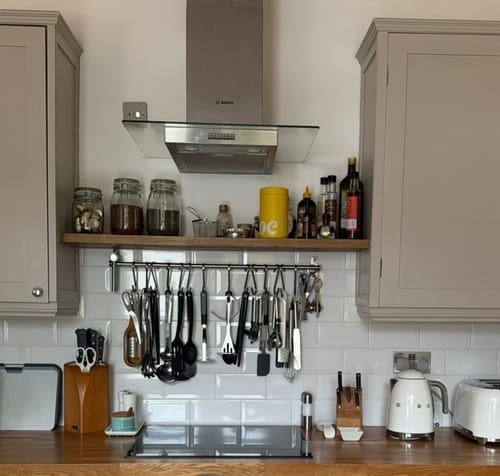 Customer's rustic floating shelf installed in a kitchen between two cabinets, holding jars and bottles.