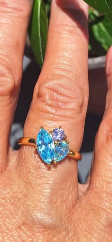 Close-up of a reviewer's hand wearing the Zia Birthstone Ring with shiny blue and lavender stones.
