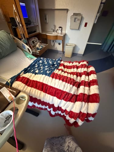Customer's plush Hugs Flag Blanket spread across their bed in a hospital room.