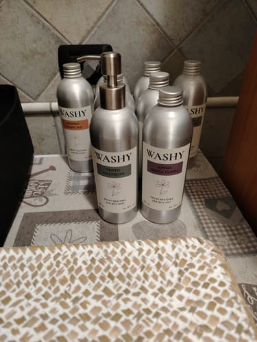 Recensore mostra diverse bottiglie argentate del profumatore Washy su un ripiano della cucina.