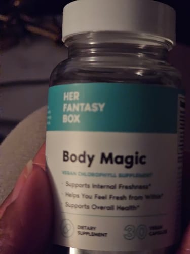 Customer's hand holding a Body Magic Chlorophyll Pill bottle with visible label text and white cap.