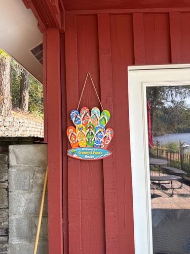 Customer's personalized wooden sign hanging on a red exterior wall at a lake cabin.