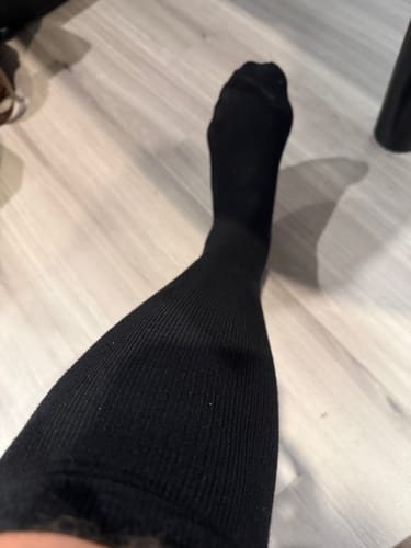 Customer's black Eucalyptus Lyocell Compression Socks worn on a leg against a wooden floor.