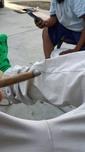 Customer's hand holding a lit Purple Milk Smalls joint while wearing a green cannabis-patterned sock outdoors.