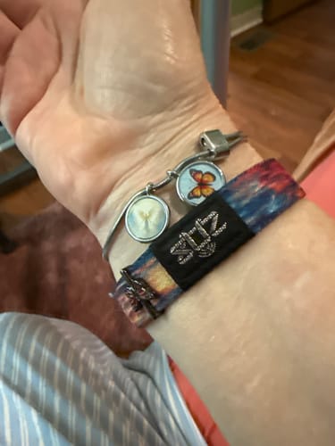 Reviewer's wrist wearing an Angel Charm Bracelet featuring a silver angel and butterfly charm, next to a fabric band.