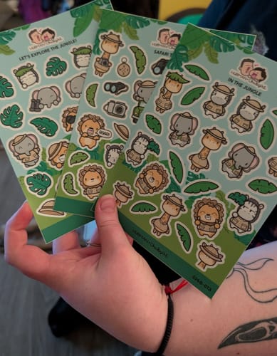 Reviewer's hand holding three sheets of green Safari-themed stickers from the Sticker Subscription.