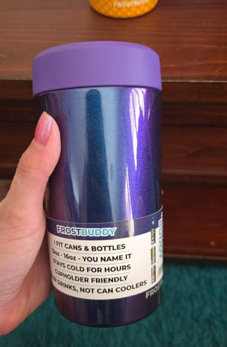 Customer's hand holding a purple Nebula Glitter Universal Buddy can cooler with product information label.