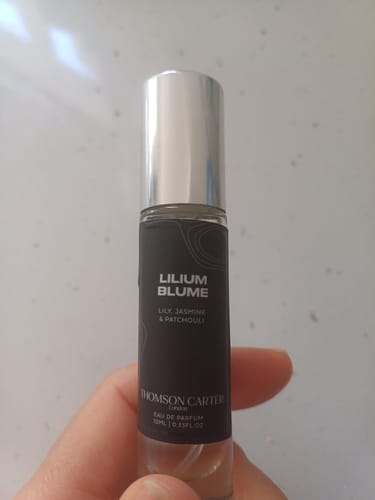 Reviewer holding a compact glass bottle of Lilium Blume Eau de Parfum with a dark label against a white background.