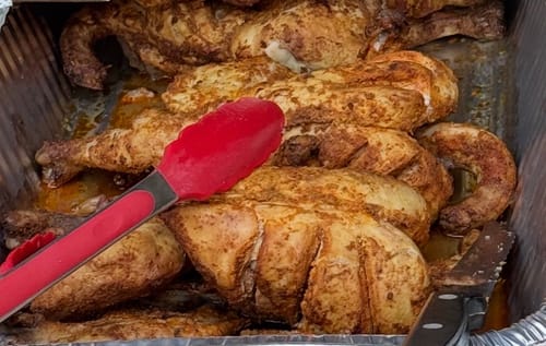 Customer's Halal Whole Chicken, seasoned and roasted in a metal tray with red tongs and a knife.