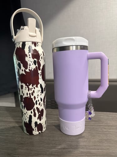 Customer's Bottle Buddy in cow print pattern next to a lavender tumbler with a charm attached.