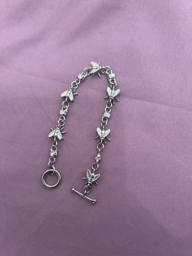 Customer's silver Rotten Bracelet featuring fly charms, laid flat on a purple fabric background.