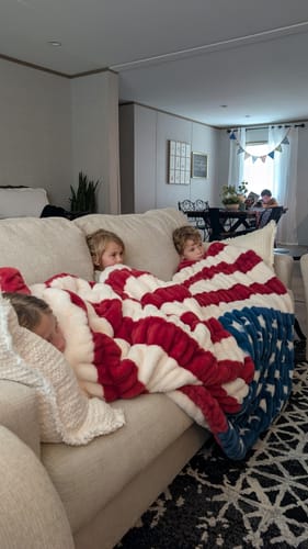 Customer's children snuggled together on a couch under the plush Hugs Flag Blanket.