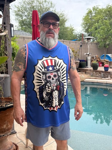 Reviewer standing outdoors wearing the blue 4th of July Calacas Basketball Jersey with its large graphic.
