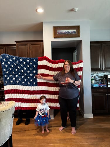 Customer and a child holding up the large, plush Hugs Flag Blanket, showing its full size indoors.