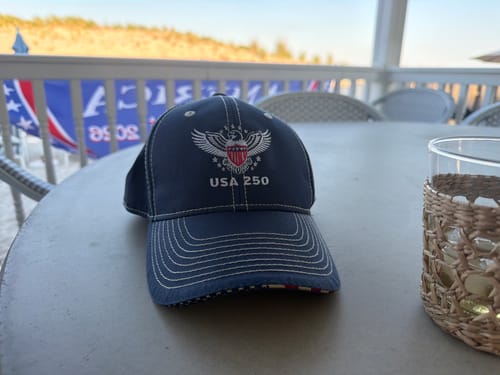 Customer's navy USA 250 Limited Edition Baseball Cap with detailed embroidery on an outdoor table.