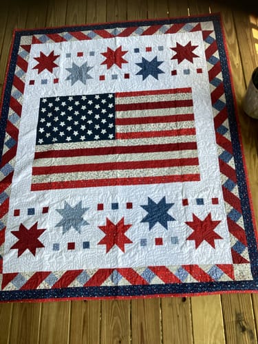 Customer's completed Freedom Song Quilt with a patriotic flag and star design, laid flat on a wooden deck.