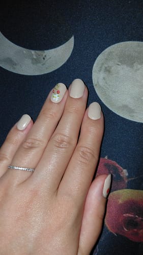 Hand einer Kundin mit einer beigen Maniküre, die mit dem dezenten UV Top Coat Gold Glitter Fine veredelt ist.