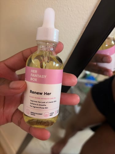 Reviewer holding the clear glass bottle of Her Fantasy Box Renew Her Yoni Oil.