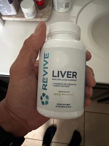 Reviewer holding a white bottle of Revive Liver support supplement in their hand in a bathroom setting.