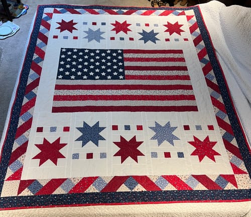 Customer's finished Freedom Song Quilt with a patriotic design spread flat on a bed.