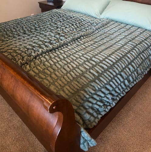 Reviewer's textured Hugs Jade Blanket spread on a bed with light green pillows.