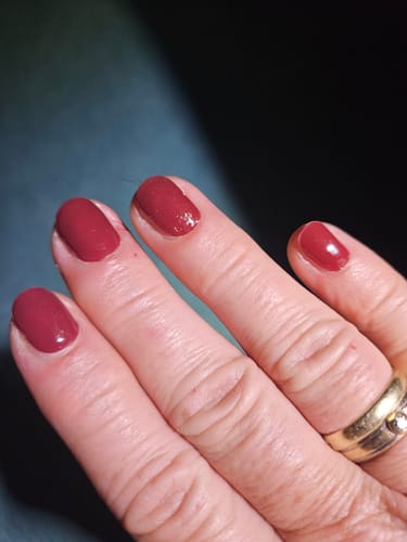 Nahaufnahme der Nägel einer Kundin, die die glänzenden, weinroten Royal Temptation UV-Gelfolien trägt.