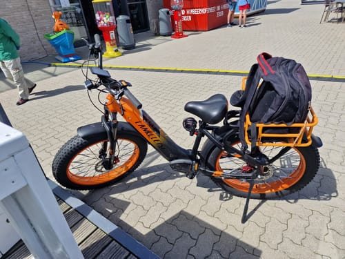 A customer's customized black and orange Lankeleisi MG600 Plus fat bike parked on a plaza with a backpack on its rear rack.