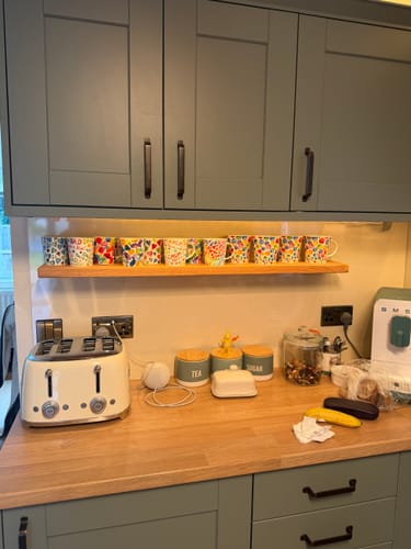 Customer's solid oak floating shelf mounted in a kitchen and displaying a row of colorful mugs.