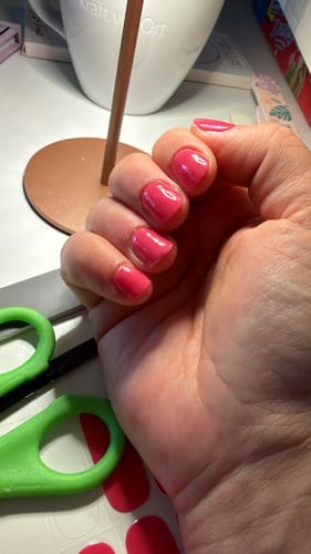 Eine Kundin zeigt ihre manikürten kurzen Nägel mit den leuchtenden „Rich Coral“ UV-Gel-Folien.