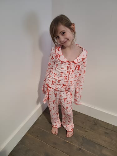 Customer's view of a smiling child wearing the P.Louise Girls Christmas Bow Pyjamas set.